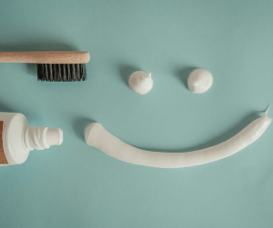Toothbrush and toothpaste arranged into a smiling face on teal background