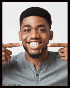 Man smiling broadly, pointing to his healthy teeth